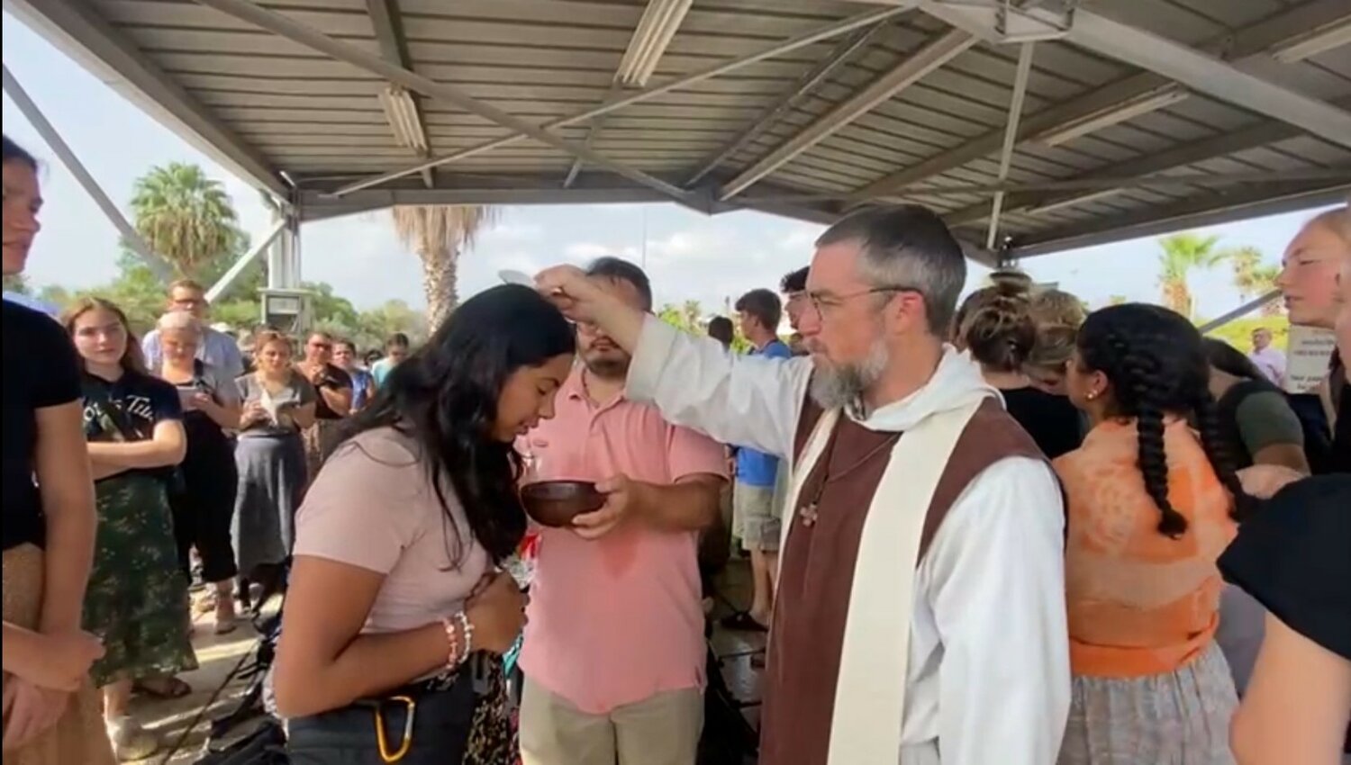 Father Anthony Ariniello, founder of the Community of the Beatitudes, who led the students on pilgrimage and served as their chaplain, renews the pilgrims’ Baptism while they waited in line for security screening at the Israel-Jordan border, on the way home from their shortened pilgrimage.
